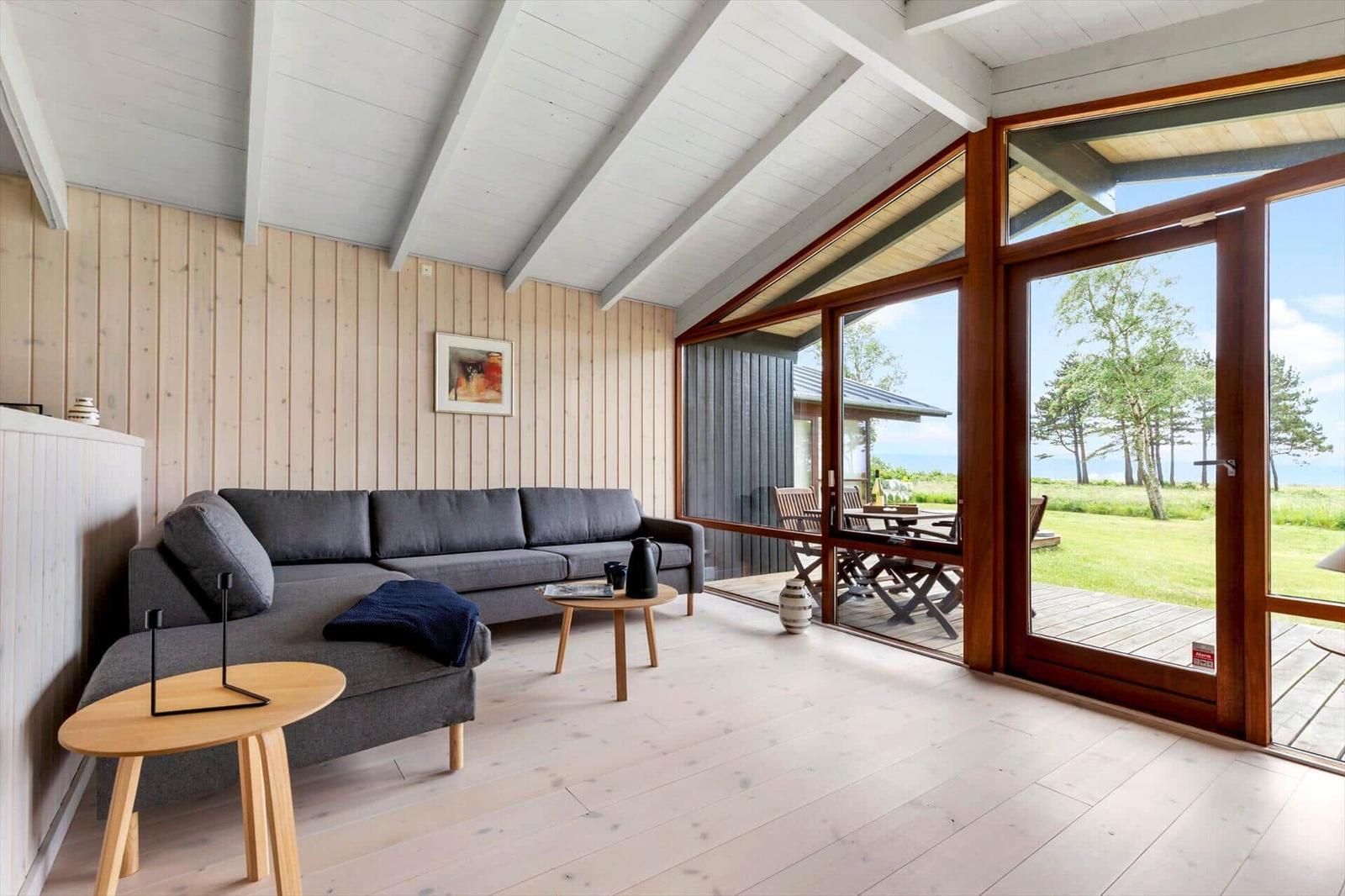 A living room with a gray sofa, wooden floor, and large windows to the terrace.