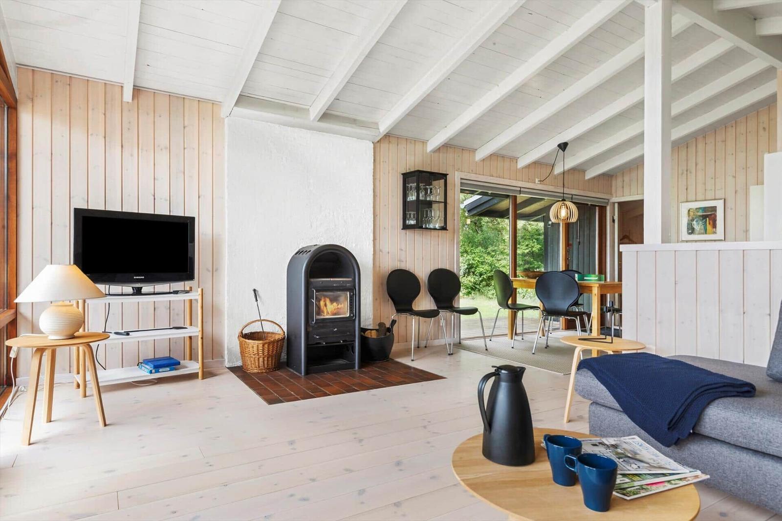 Living room with fireplace, TV, and dining area. Wooden floors and white ceiling beams.