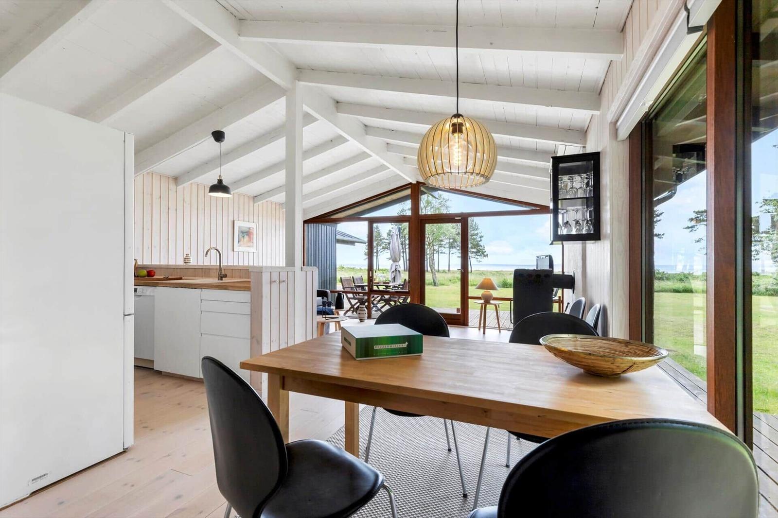 Dining area with table and chairs. Kitchen and terrace with view of green field.