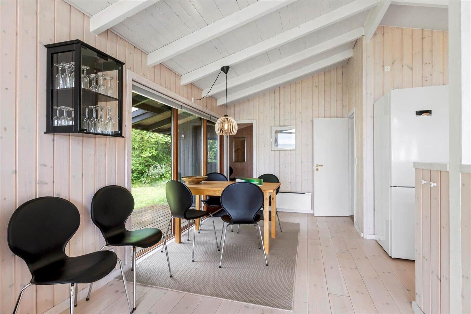 Dining room with wooden walls, table, chairs, and glass door to garden.
