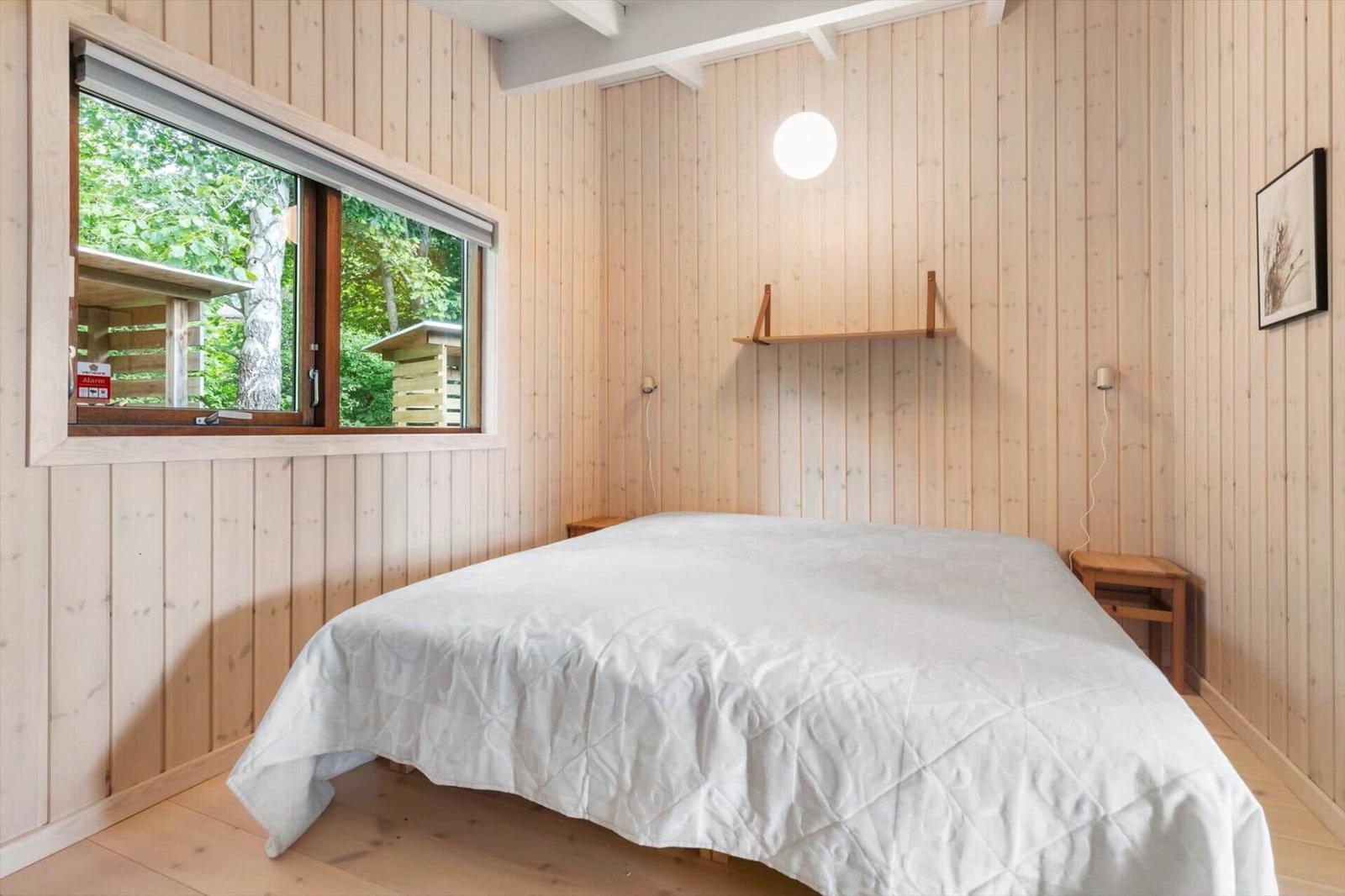 Bedroom with wood walls, bed, and window view of forest.