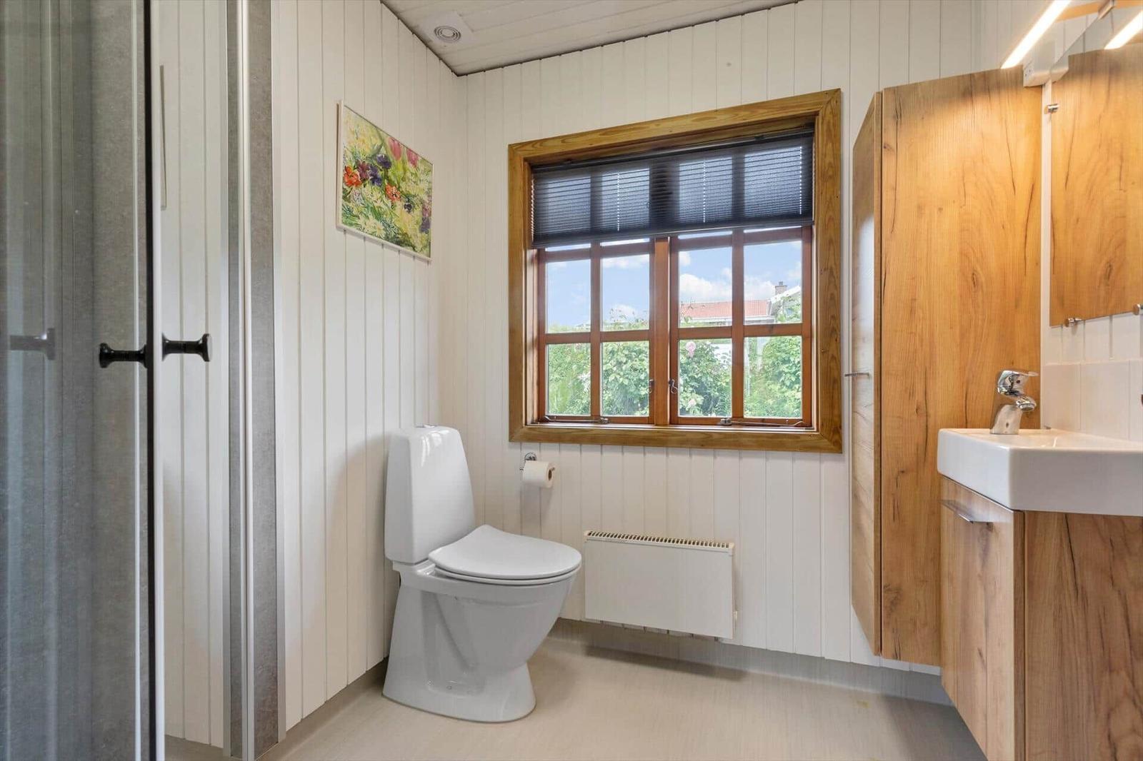 Badezimmer mit Toilette, Waschbecken und Dusche. Holzfenster und Wandpaneelen.