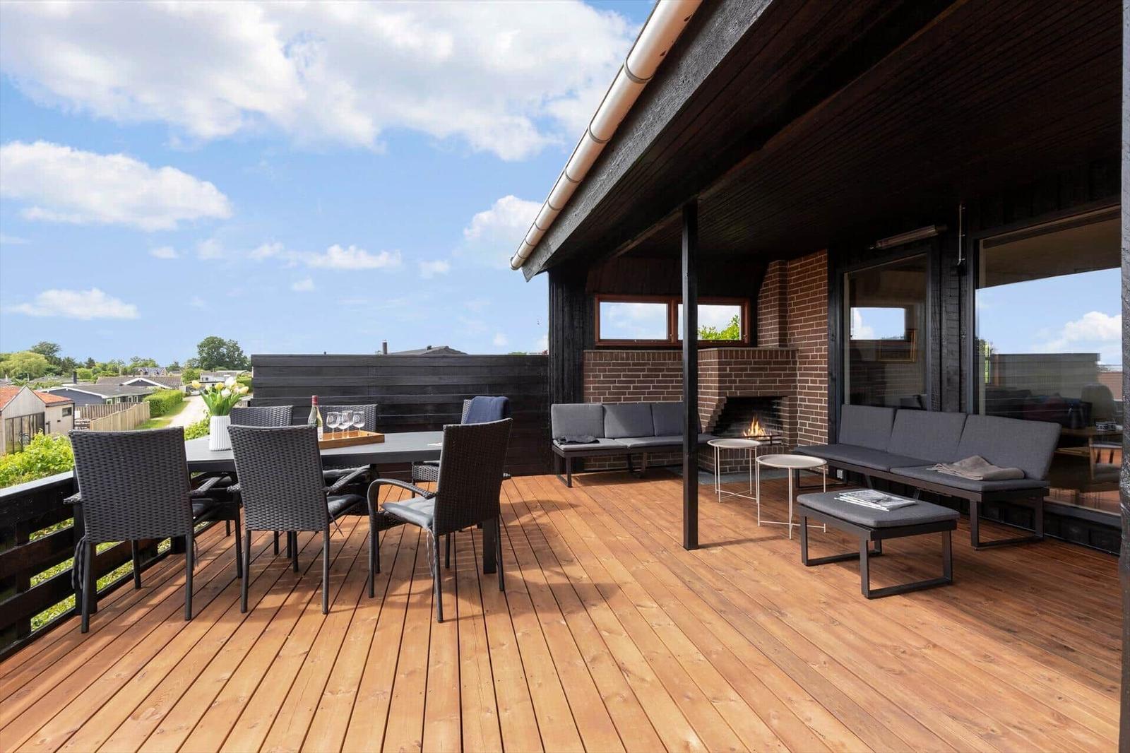 Terrasse mit Sitzgruppe, Esstisch und Kaminofen. Holzdecke und Blick auf die Umgebung.