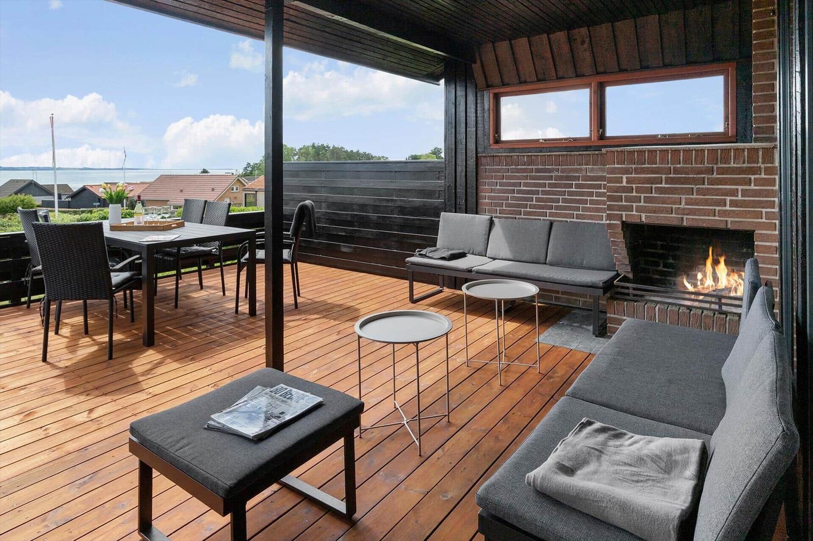 Terrasse mit Sitzgelegenheiten, Grillplatz und Blick auf Wasser.