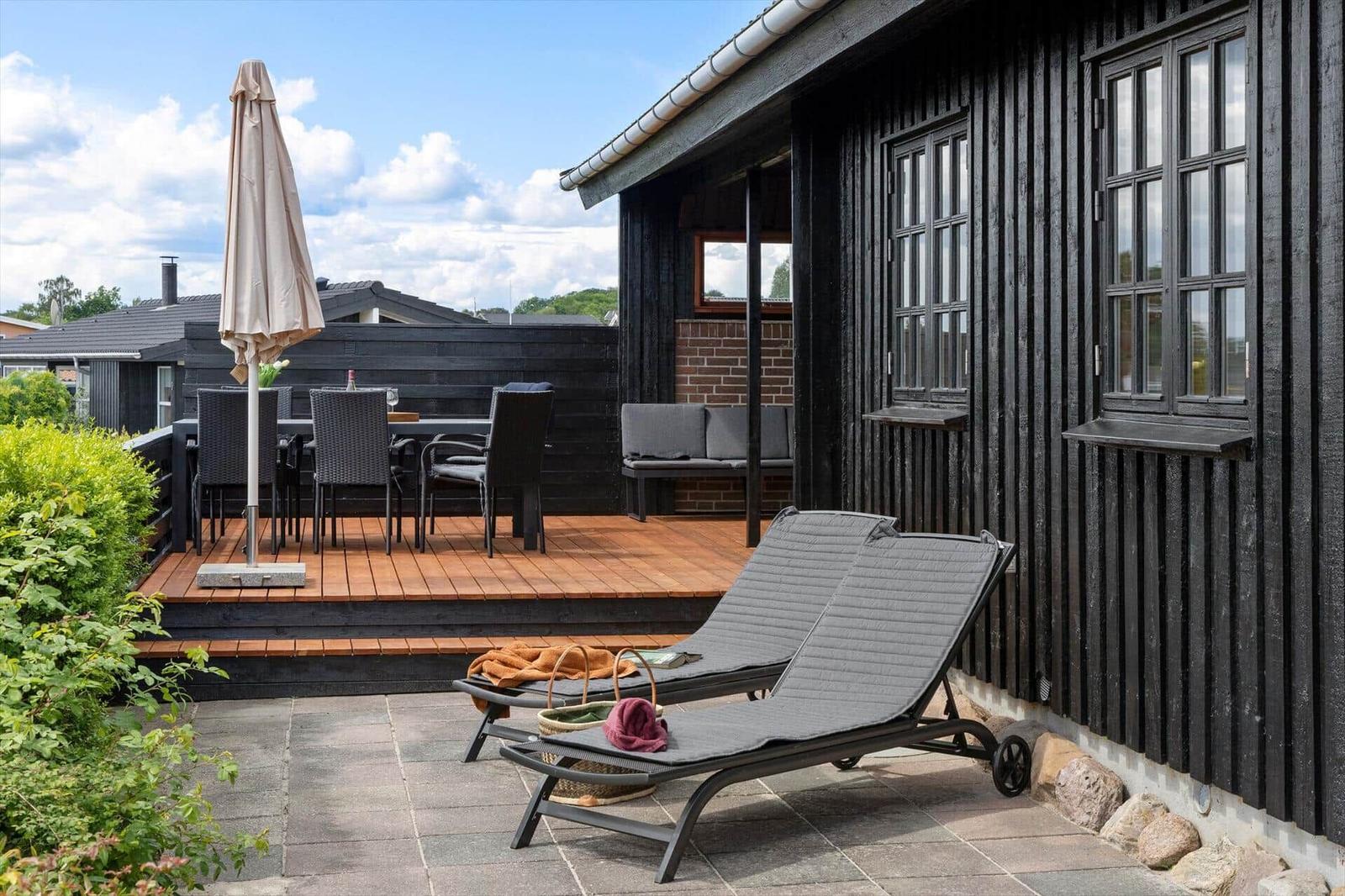 Terrasse mit Liegestühlen, Tisch und Stühlen neben einem schwarz gestrichenen Haus.