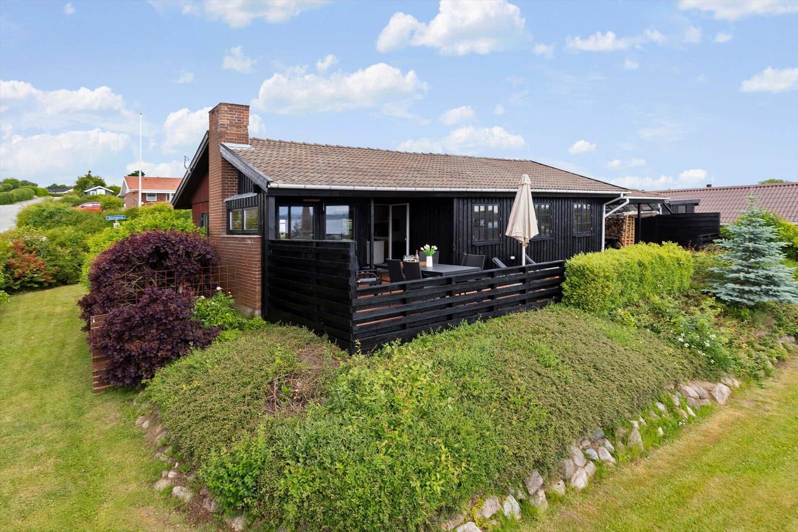 Schwarzes Holzhaus mit Terrasse, Garten und Blick auf Wasser.
