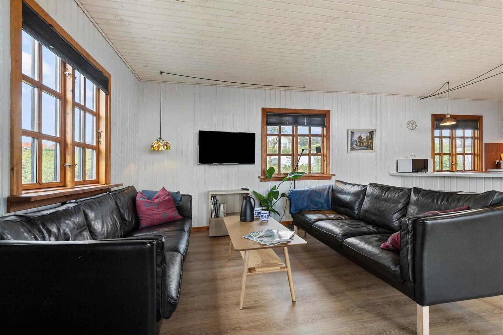 Wohnzimmer mit zwei schwarzen Ledersofas, Holztisch und Fenstern mit Holzrahmen.