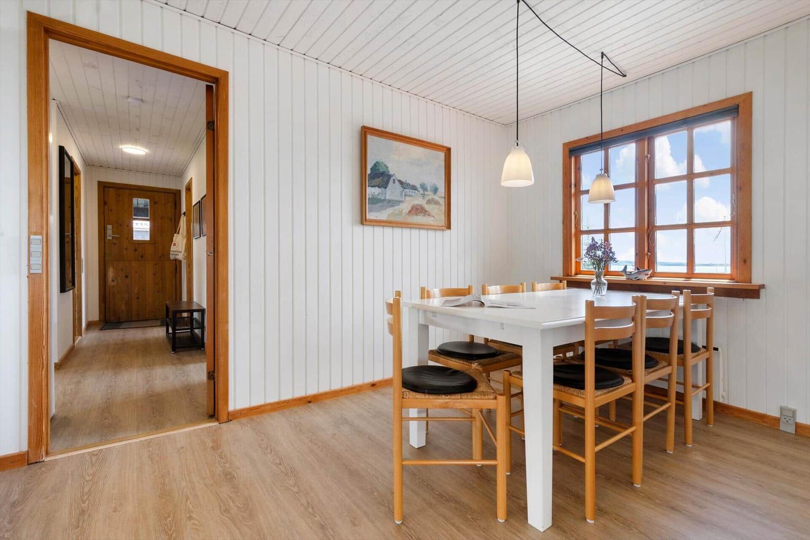 Esszimmer mit Tisch, Stühlen und Fenster. Durchgang zum Flur mit Holztür.