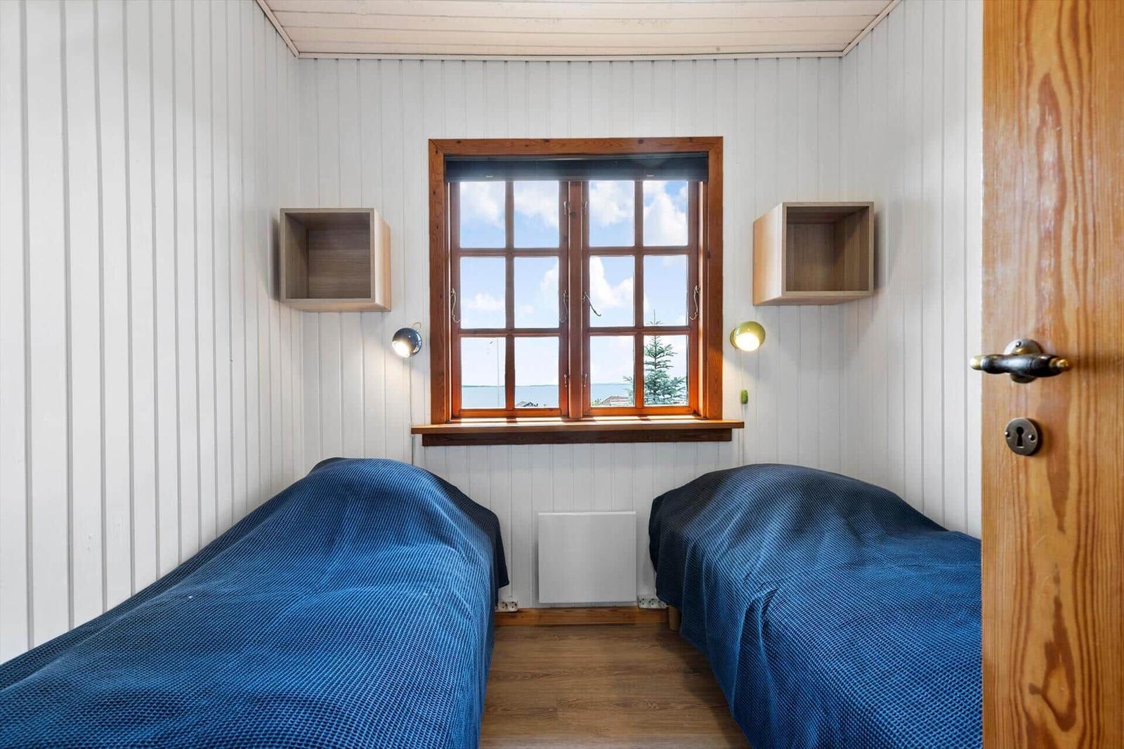 Zwei Betten mit blauen Bettdecken, Fenster mit Blick aufs Meer, Holzwand und Schränke.