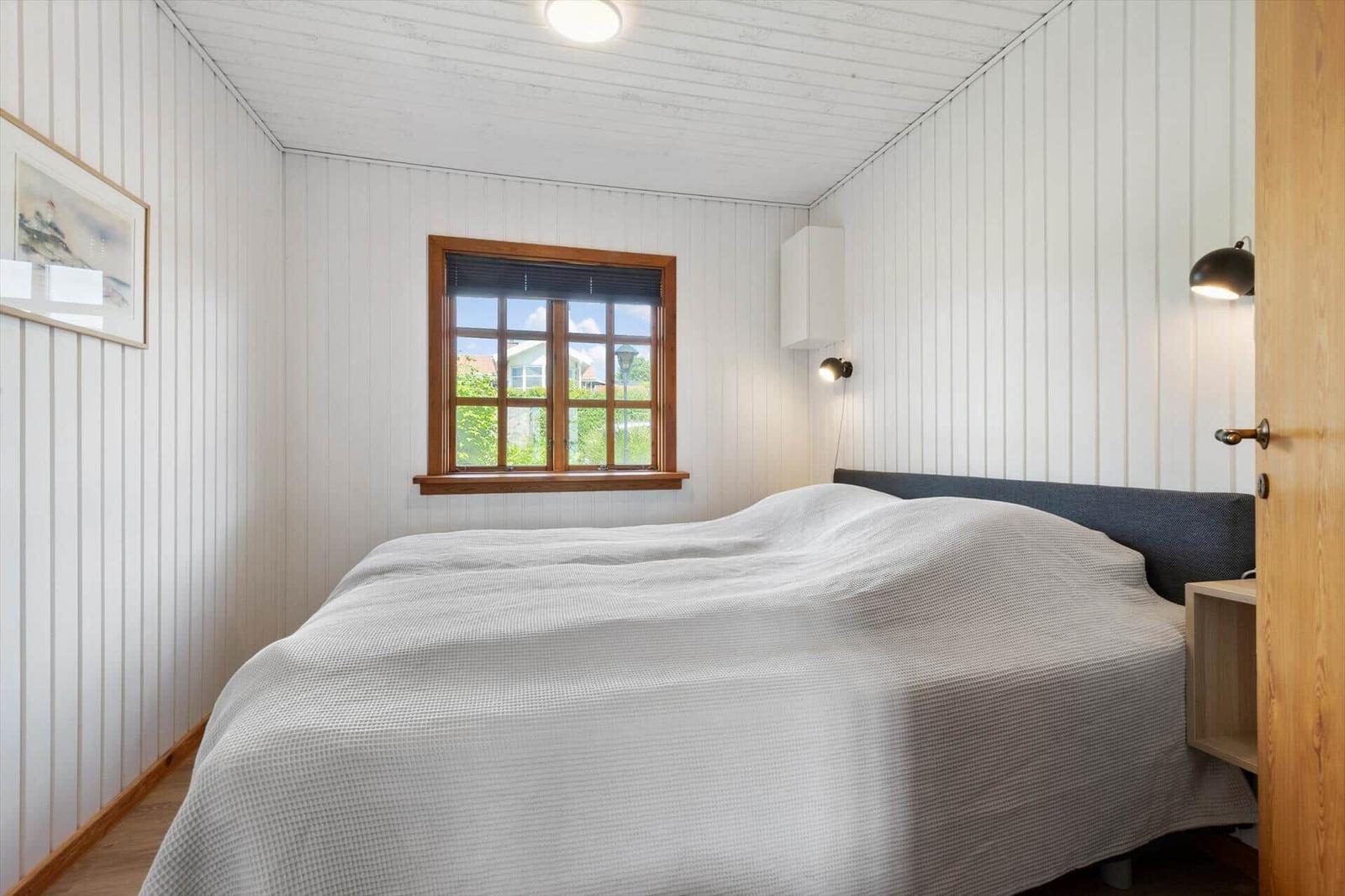 Schlafzimmer mit Bett, Fenster und Wandlampen.