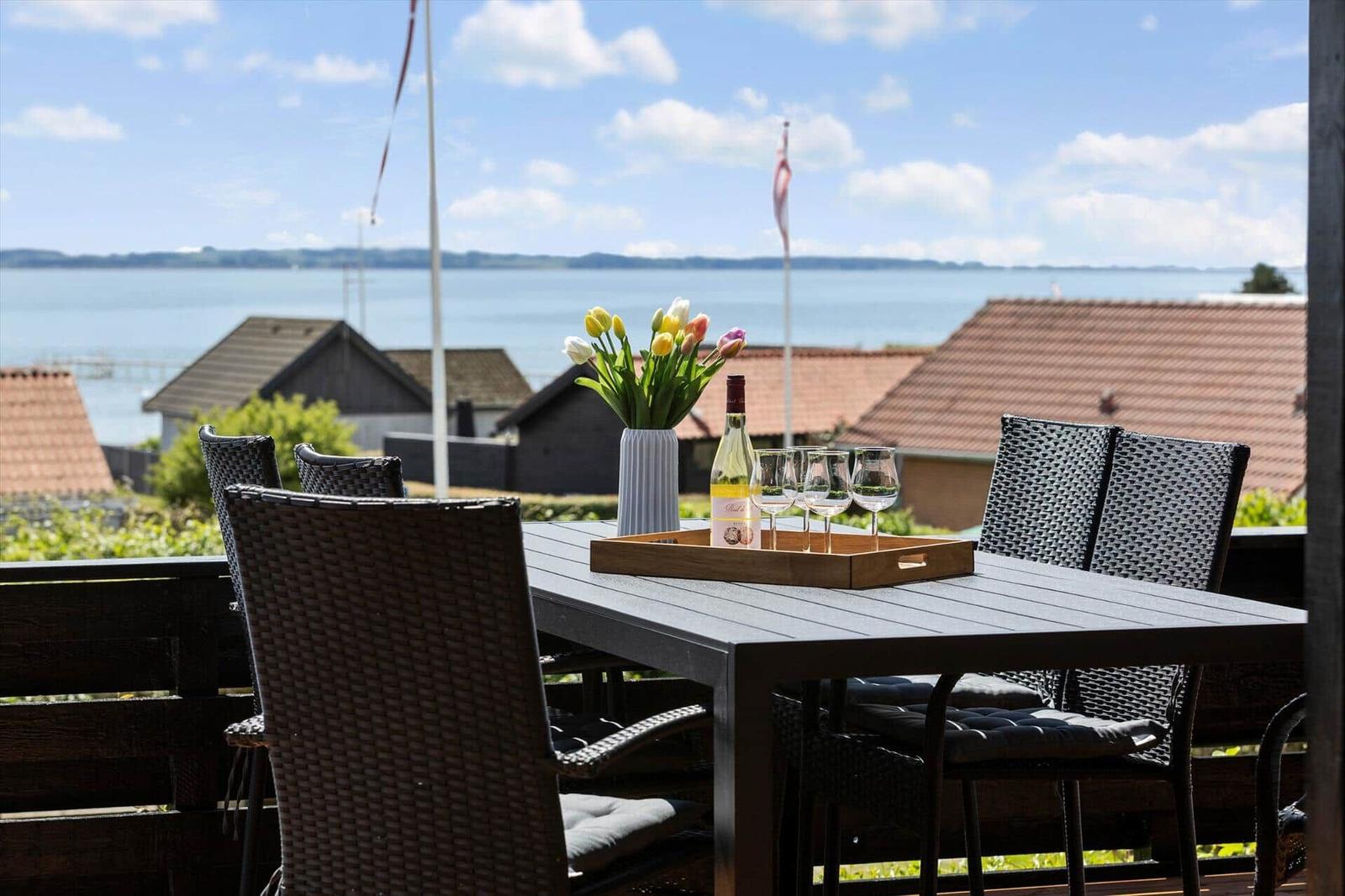 Terrasse mit Tisch, Stühlen und Blumen. Blick auf Wasser und Häuser.