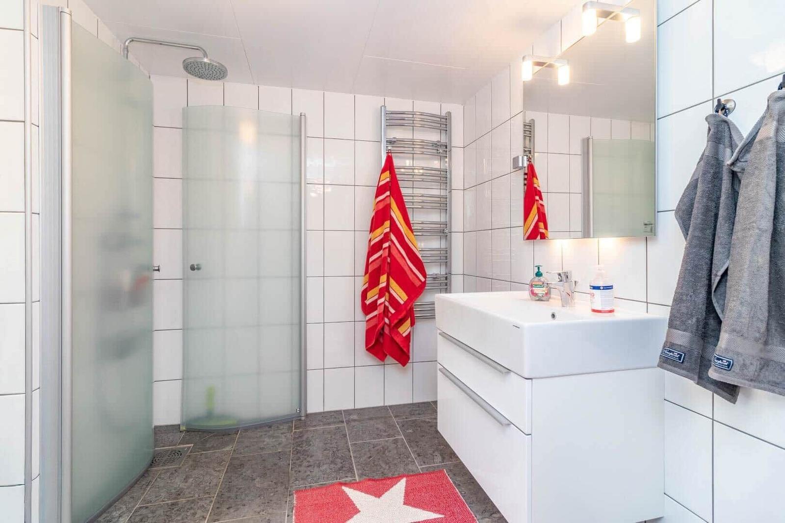 Badezimmer mit Dusche, Waschbecken und Handtüchern an Wänden.