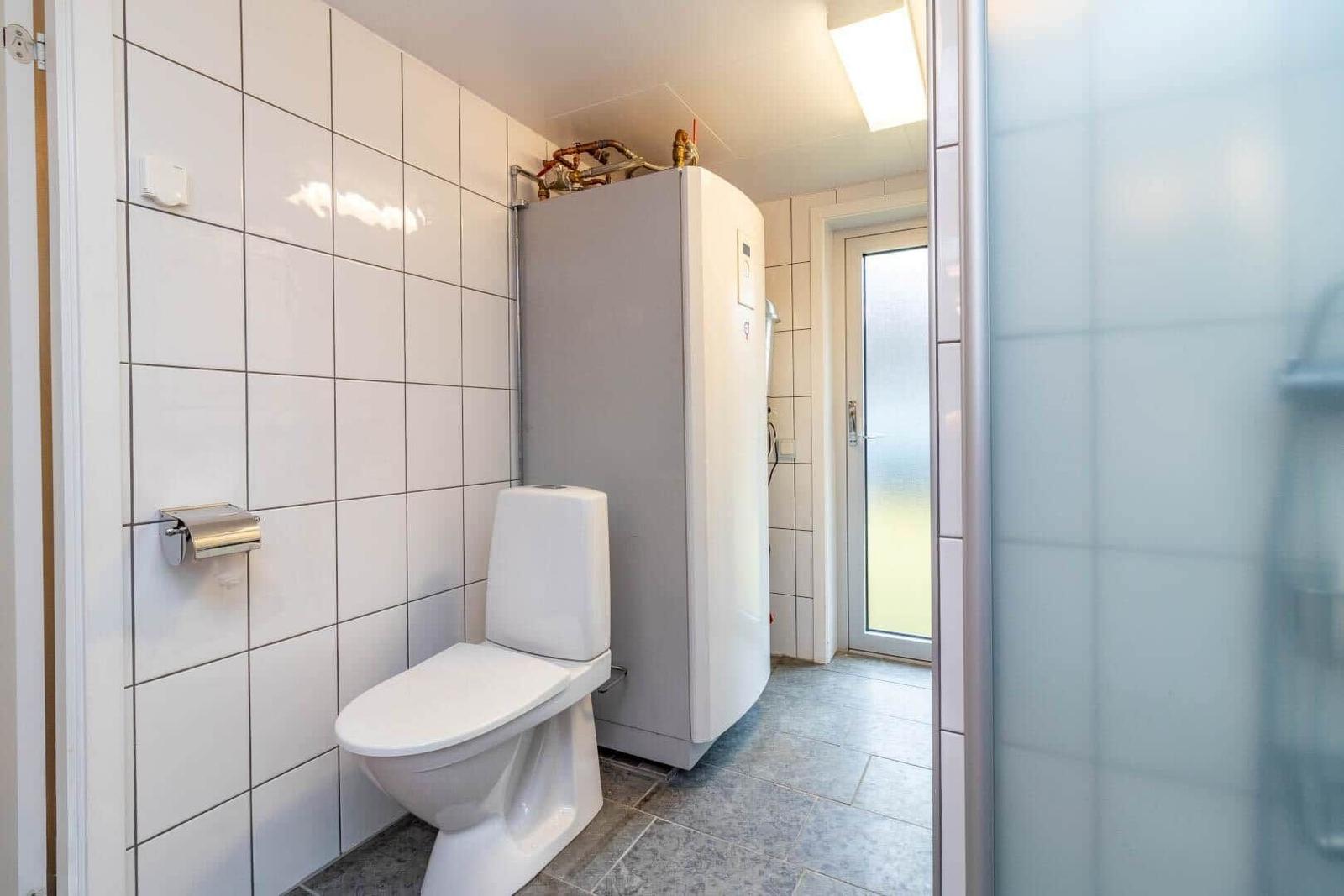 Bad mit Toilette, Duschbereich und Heizungsgerät an der Wand.