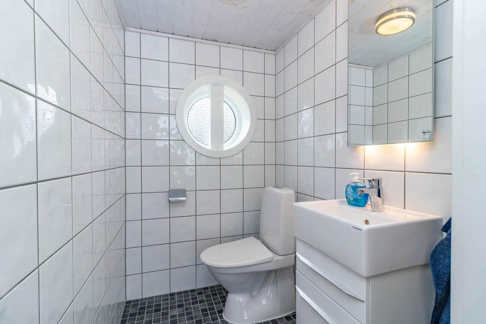 Badezimmer mit Toilette, Waschbecken und runden Fenster. Fliesenwand und Spiegel.
