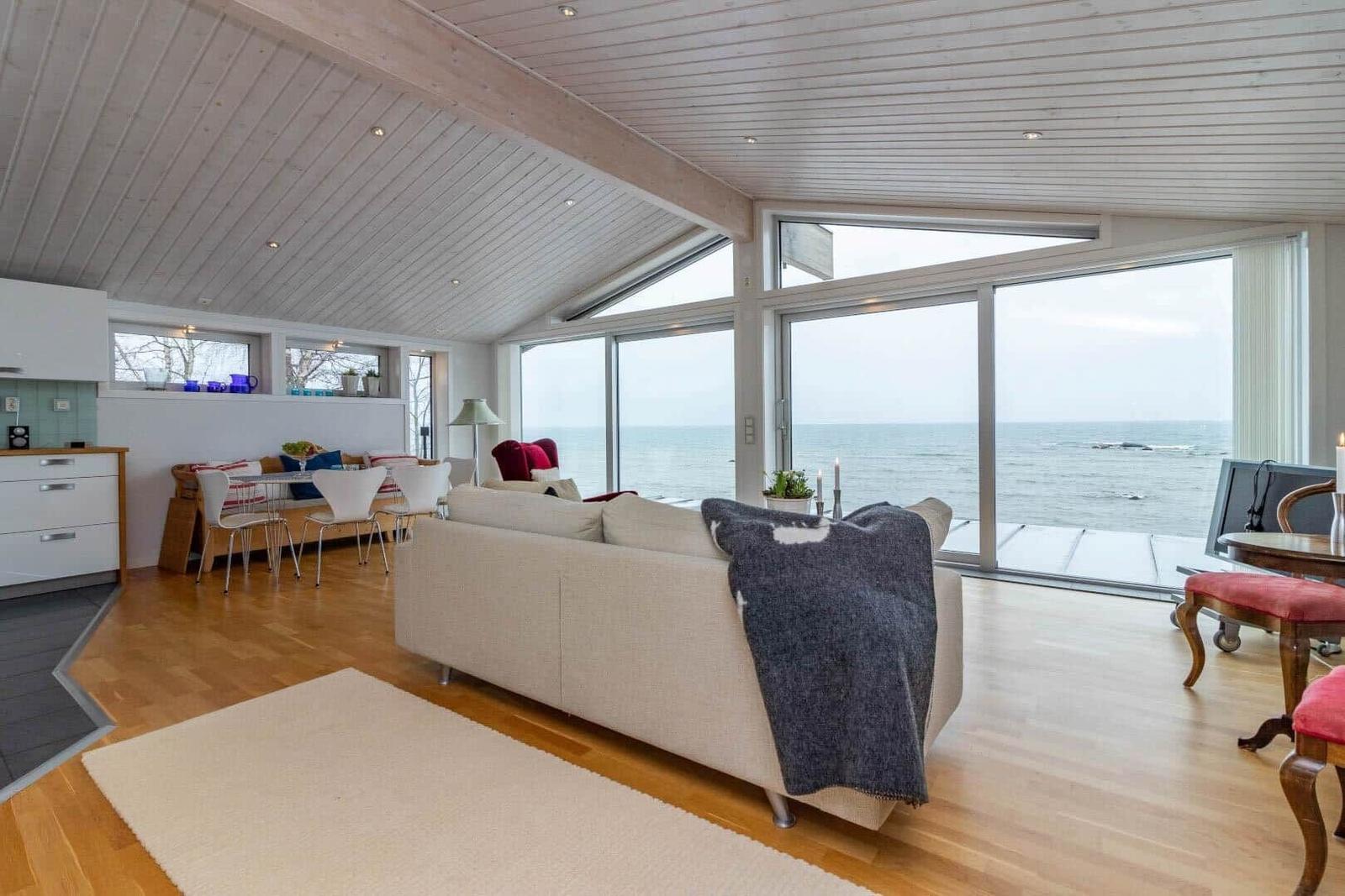 Wohnbereich mit Küchenzeile, Sofa und Blick aufs Meer durch große Fenster.
