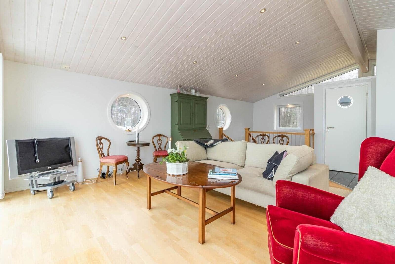 Wohnzimmer mit Sofa, rotem Sessel, Holztisch und Rundfenstern.