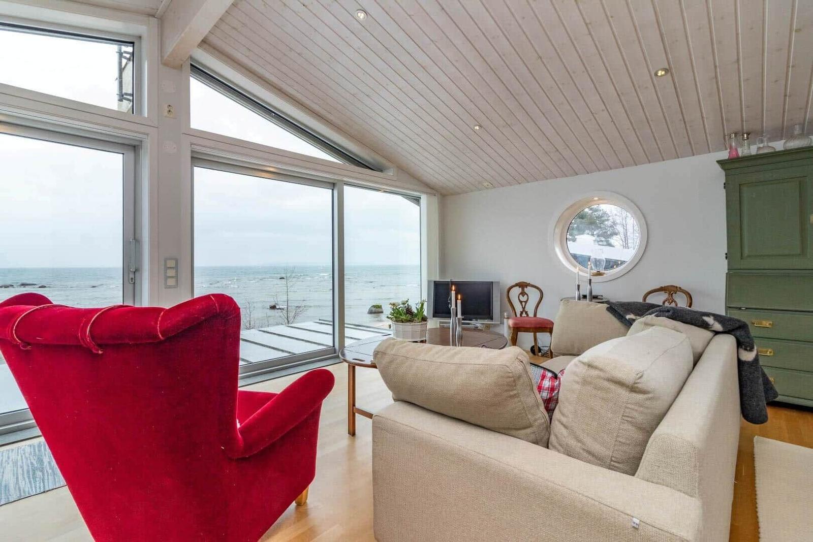 Wohnzimmer mit Blick aufs Meer, roter Sessel, Sofa und runde Fenster.