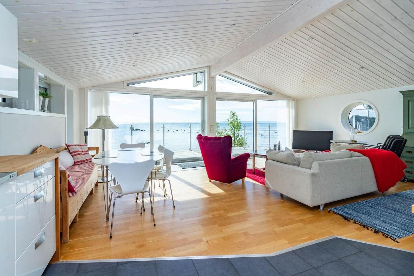 Wohnraum mit Küchenbereich, Blick aufs Meer, rote Sessel und Sofa.