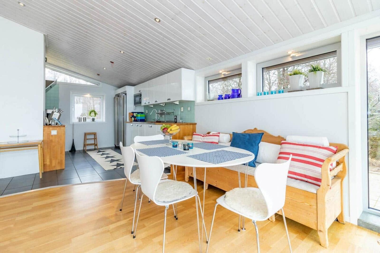 Essbereich mit Tisch, Stühlen und Sofa. Küche im Hintergrund. Holzboden und weiße Wände.
