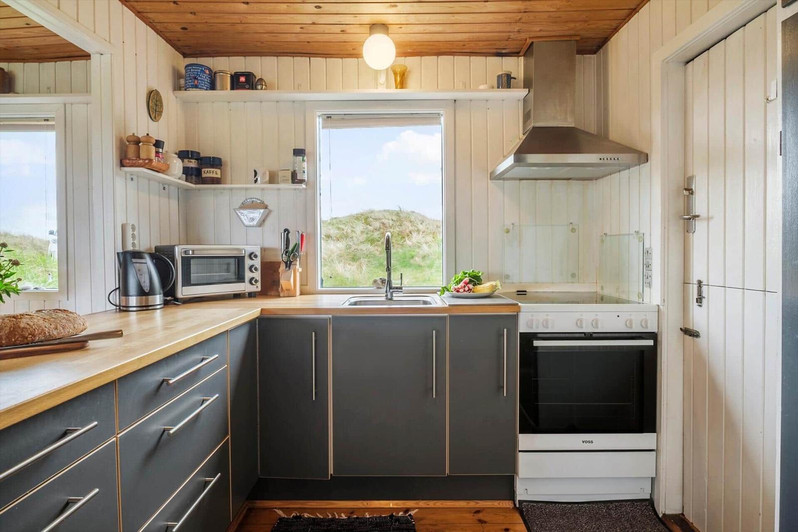 Küche mit dunklen Schränken, Holzoberfläche und Fensterblick auf Grünland.