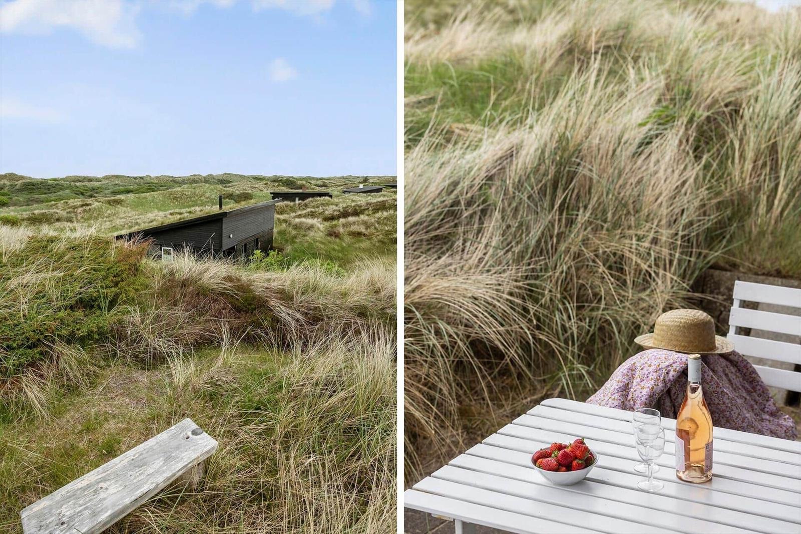 Holzhaus in Dünenlandschaft mit weißem Tisch und Stuhl. Tisch mit Erdbeeren und Roséwein.