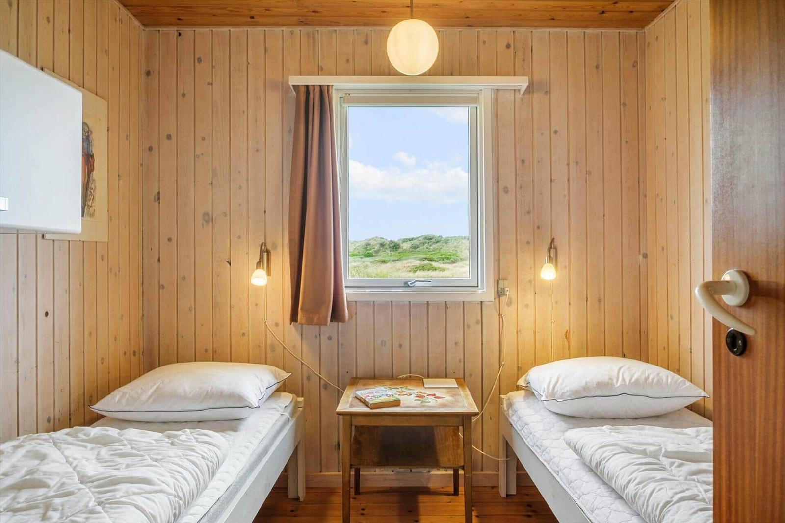 Zwei Einzelbetten, kleiner Tisch und Fenster mit Blick auf die Dünen.