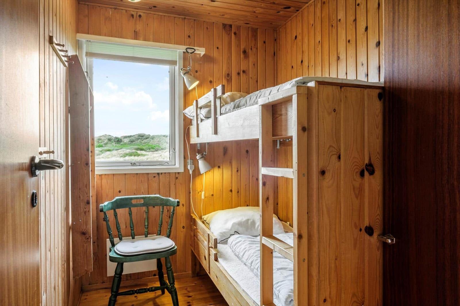 Zimmer mit Doppelstockbett, grüner Stuhl und Fensterblick auf Dünen.