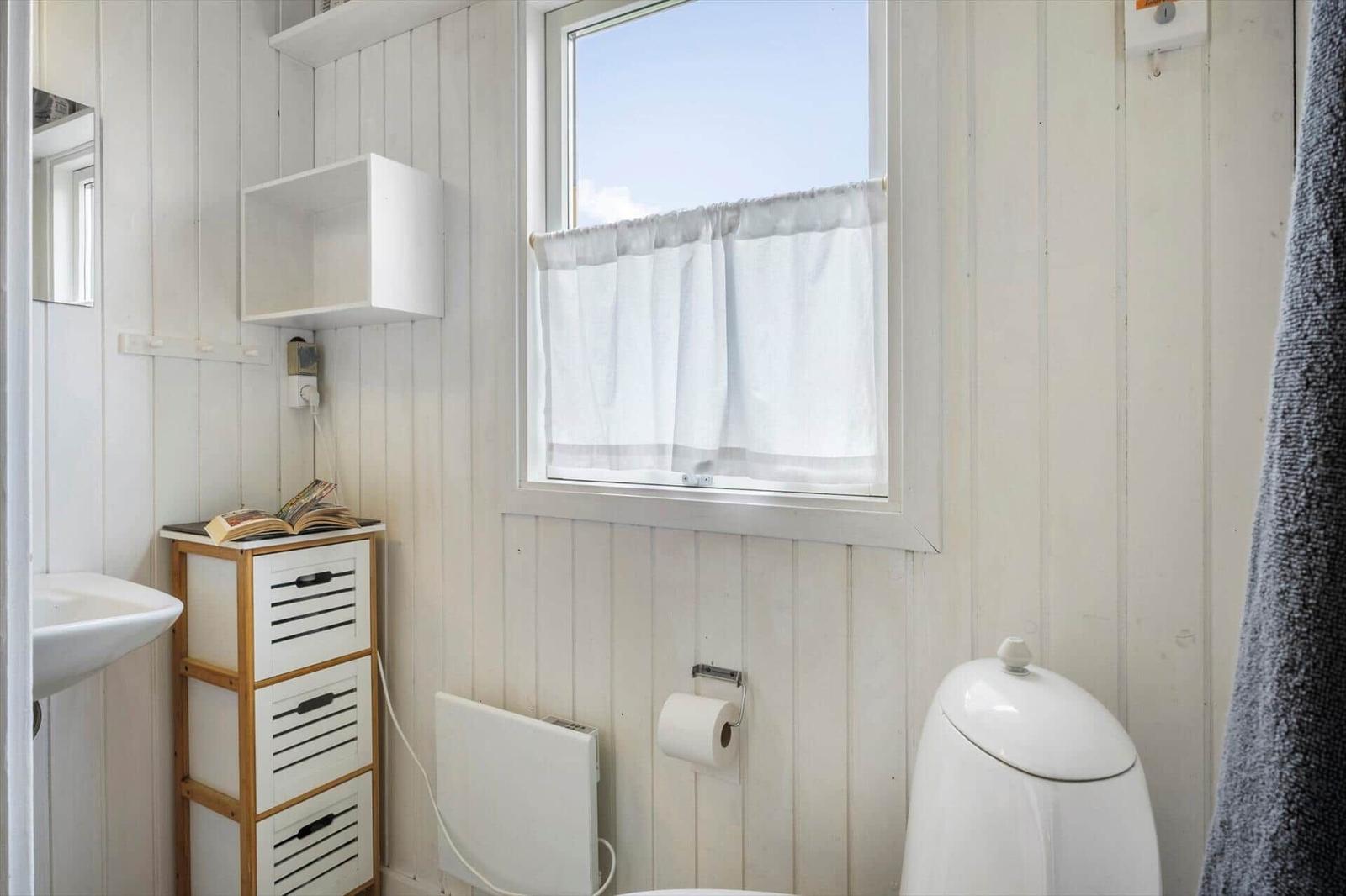 Badezimmer mit Toilette, Waschbecken und Fenster mit weißen Vorhängen.