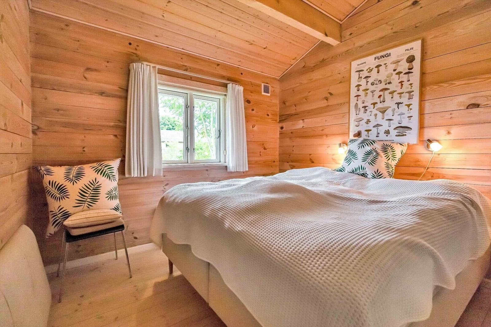 Bedroom with wooden walls, bed, window, and mushroom poster on the wall.
