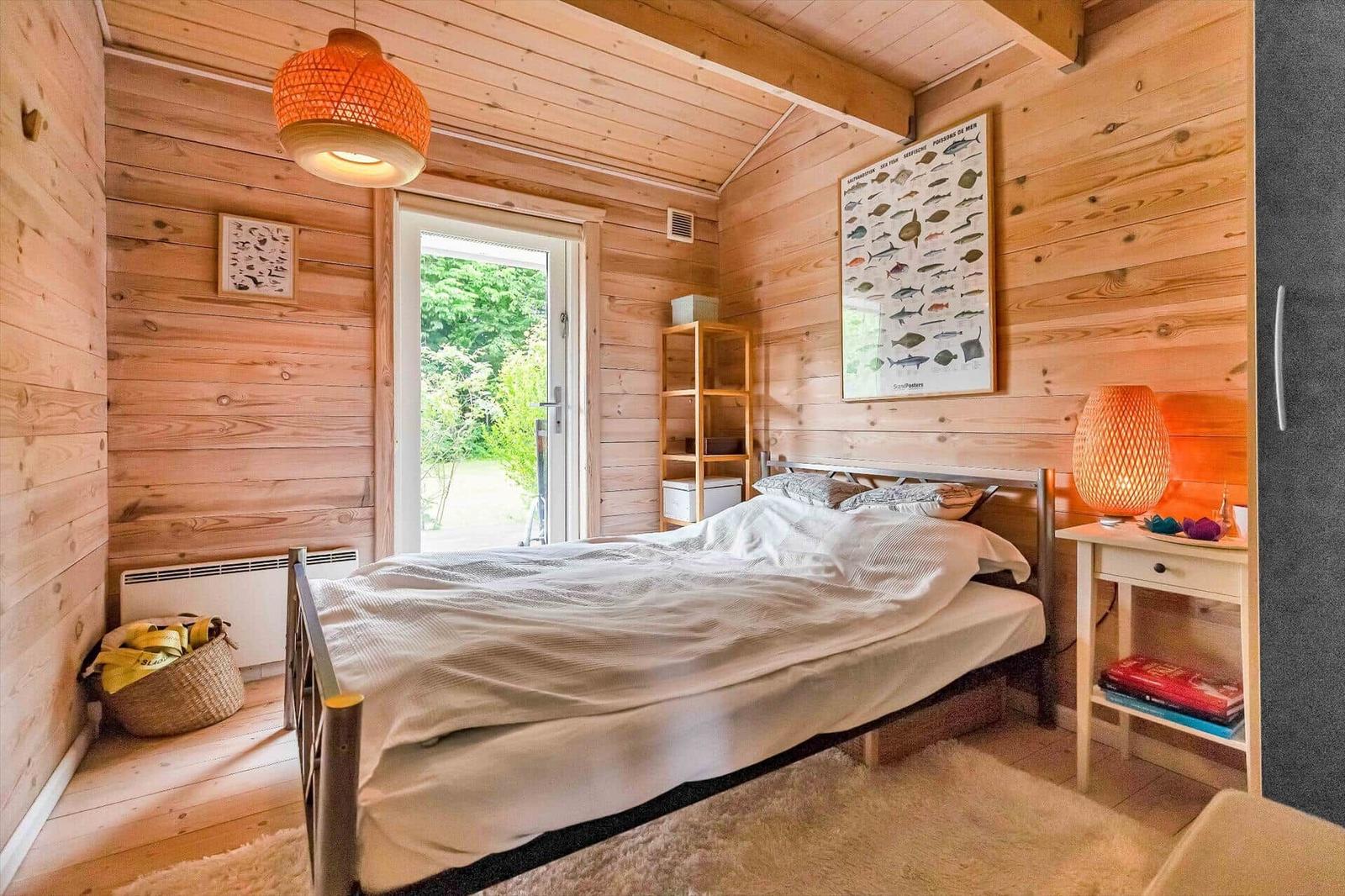 Bedroom with wooden walls, bed, nightstand, and door to the garden.