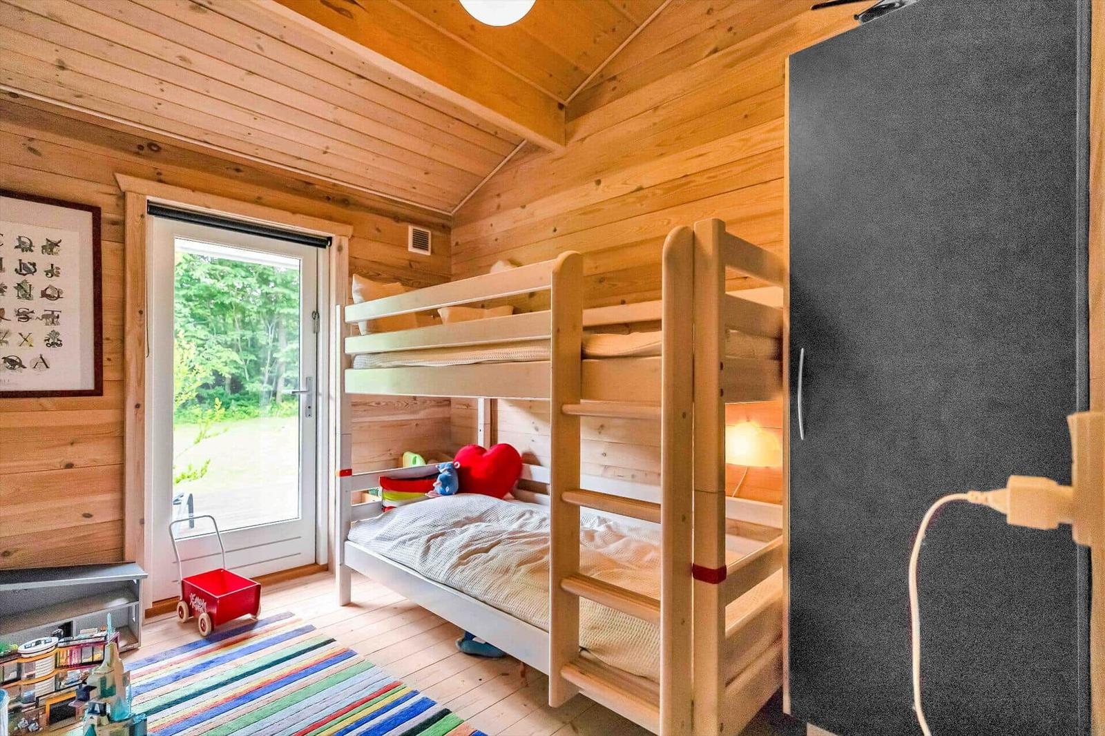 A bedroom with bunk bed, wooden walls, and door to the garden.