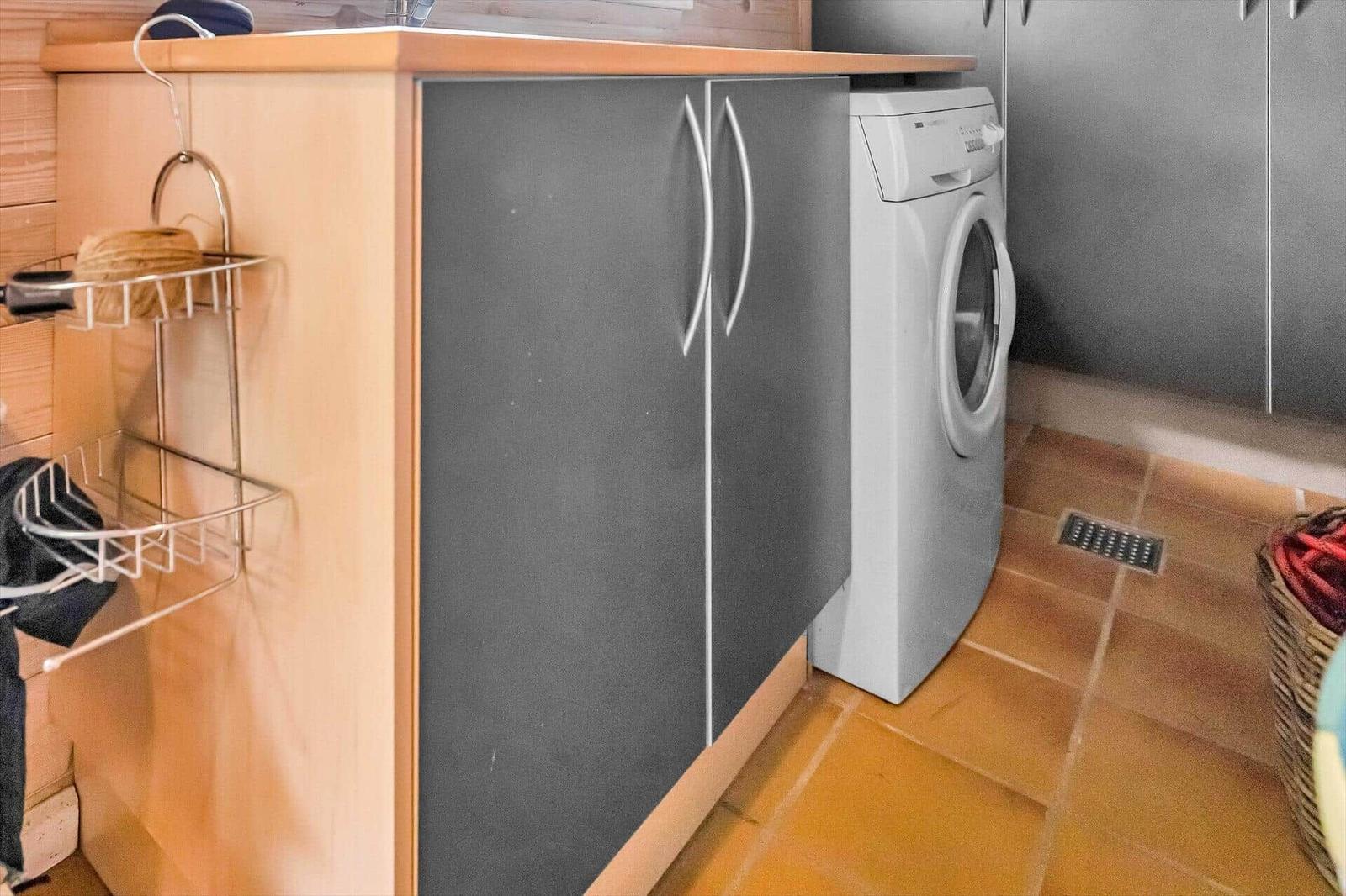 Washing machine next to kitchen cabinets with wooden top and metal rack.