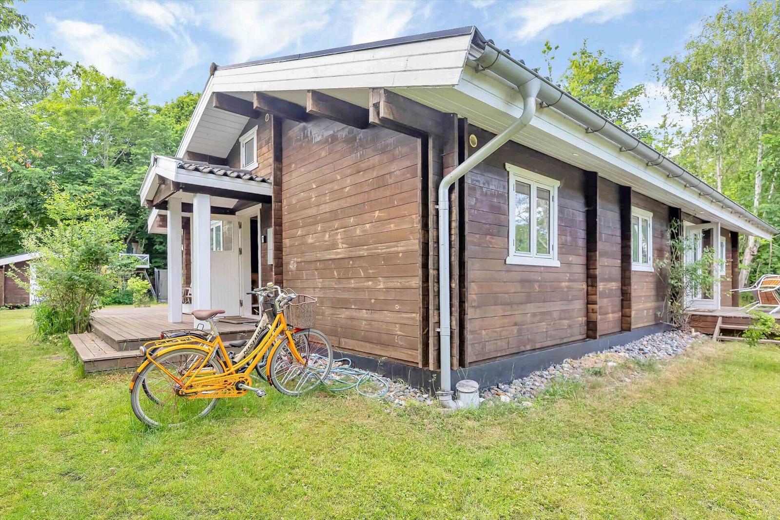 Wooden house with terrace, bicycle, and lawn. Windows and roof details visible.