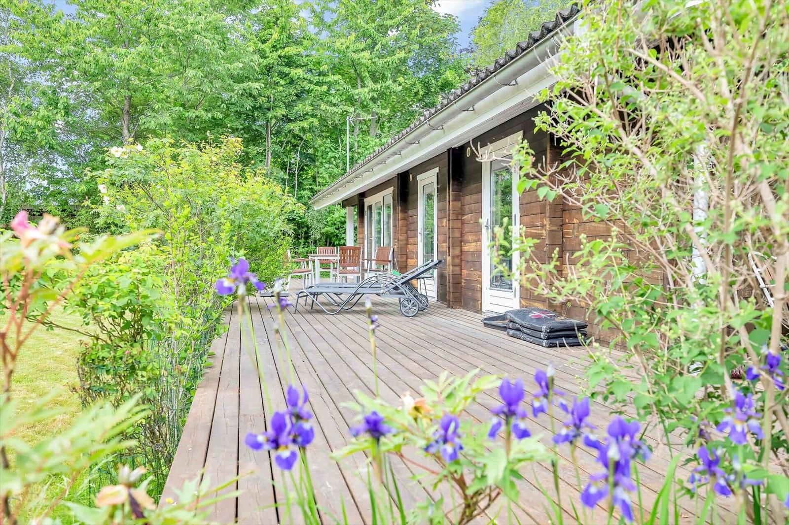 Wooden terrace with lounge chairs and flowers in front of a wooden house.