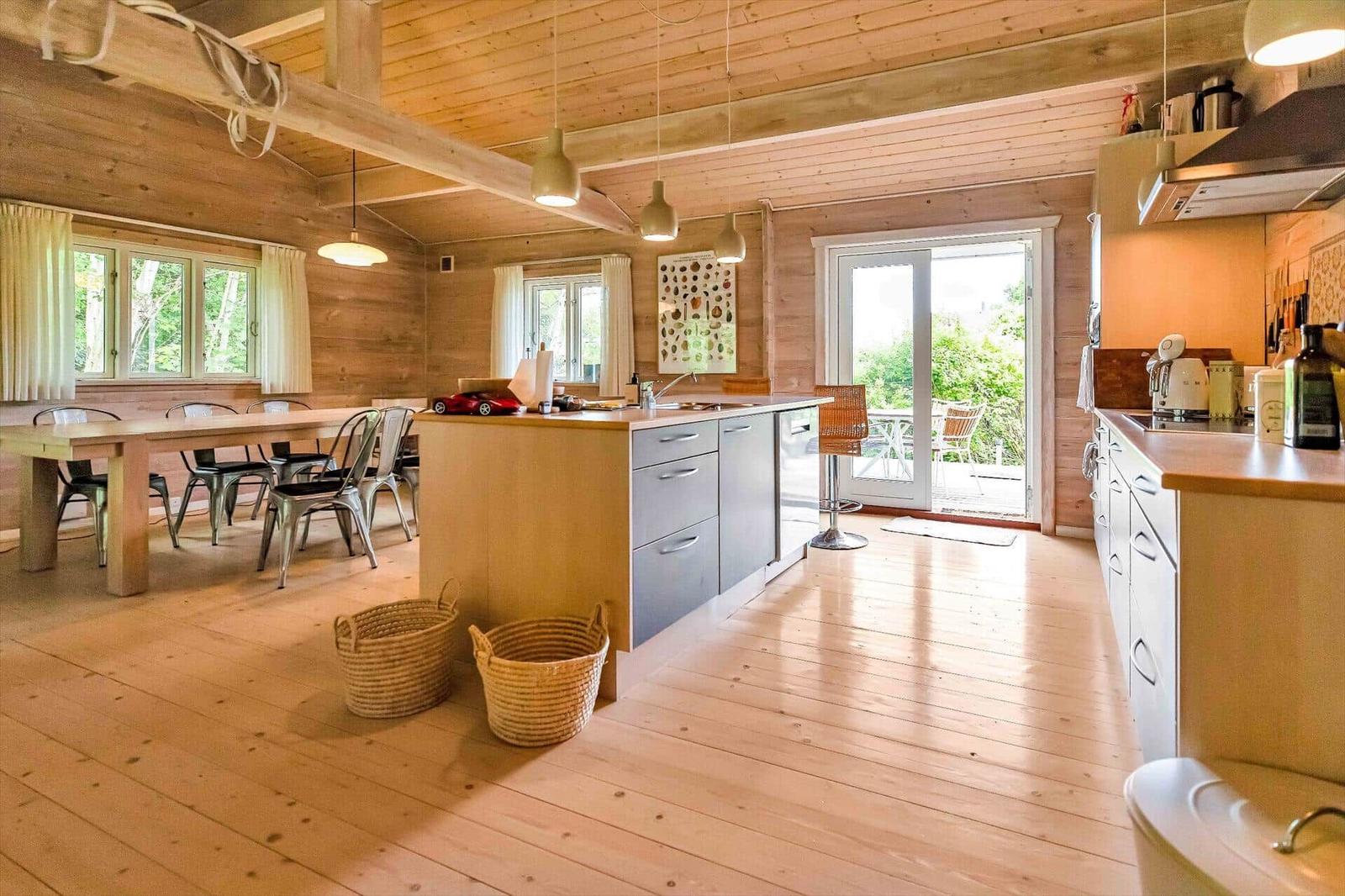 Kitchen and dining area with wooden floor, ceiling, and walls. Windows and glass door lead to the terrace.