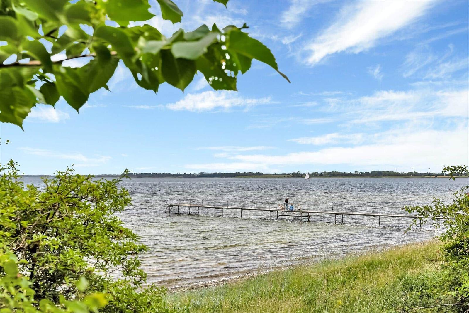 A dock extends into the water. In the background, a sailboat sails under a blue sky.
