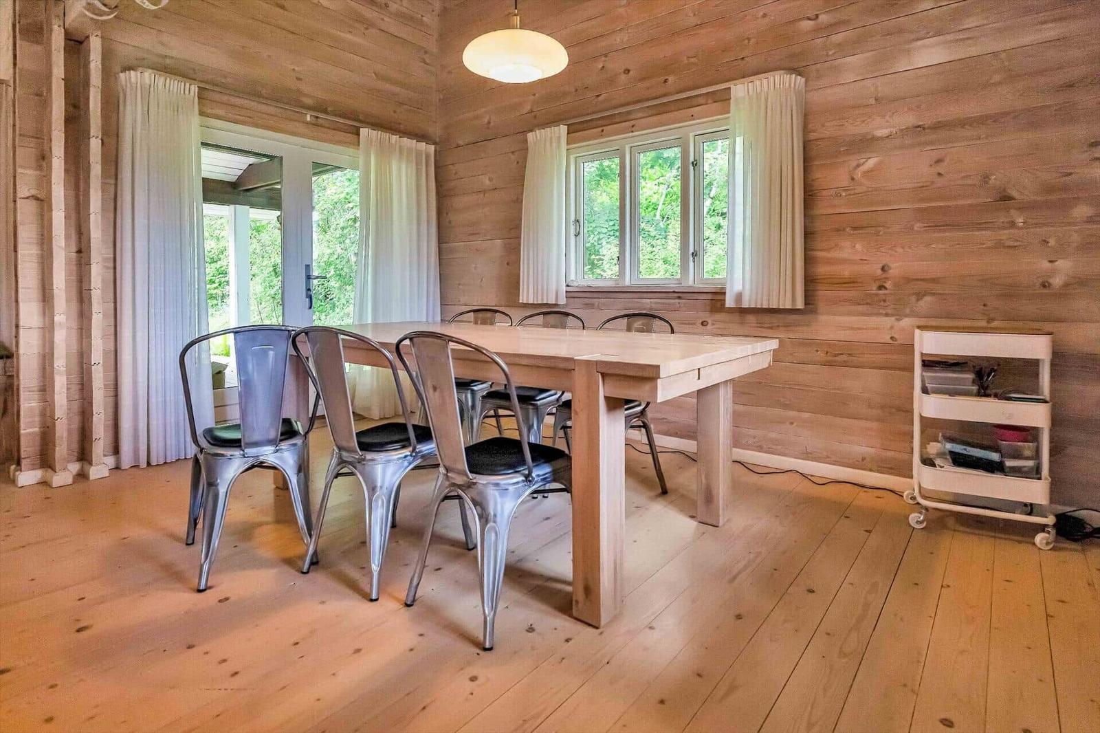 Dining room with wooden walls, table, and metal chairs. Windows and glass door show greenery.