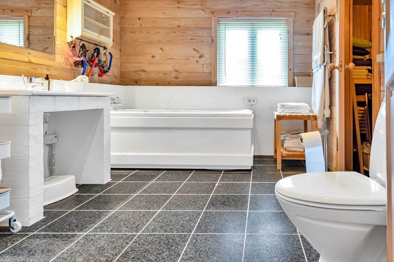 Bathroom with bathtub, toilet, and sink. Wooden walls and tiled floor.