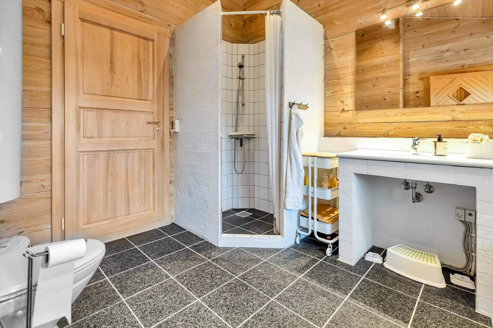 Bath with shower, sink, and toilet. Wooden walls and tiled floor.
