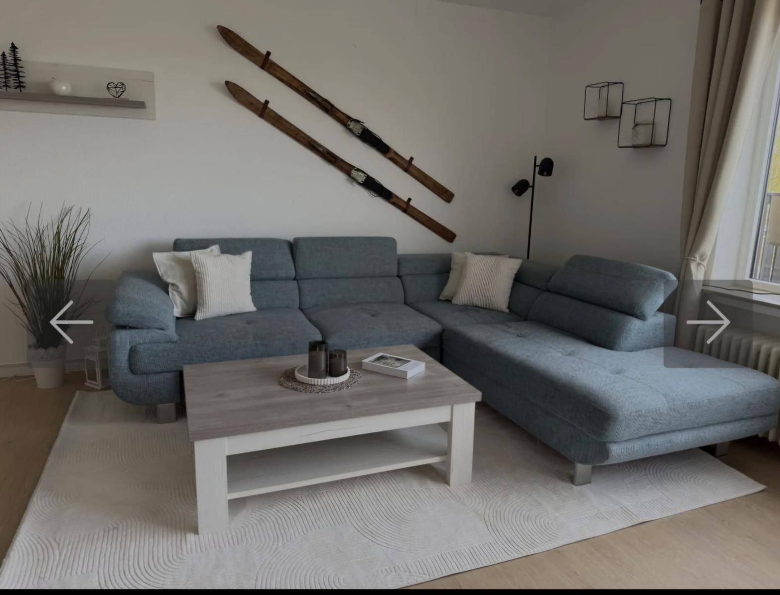 Ein Wohnzimmer mit grauem Sofa, Holztisch und Skiern an der Wand.