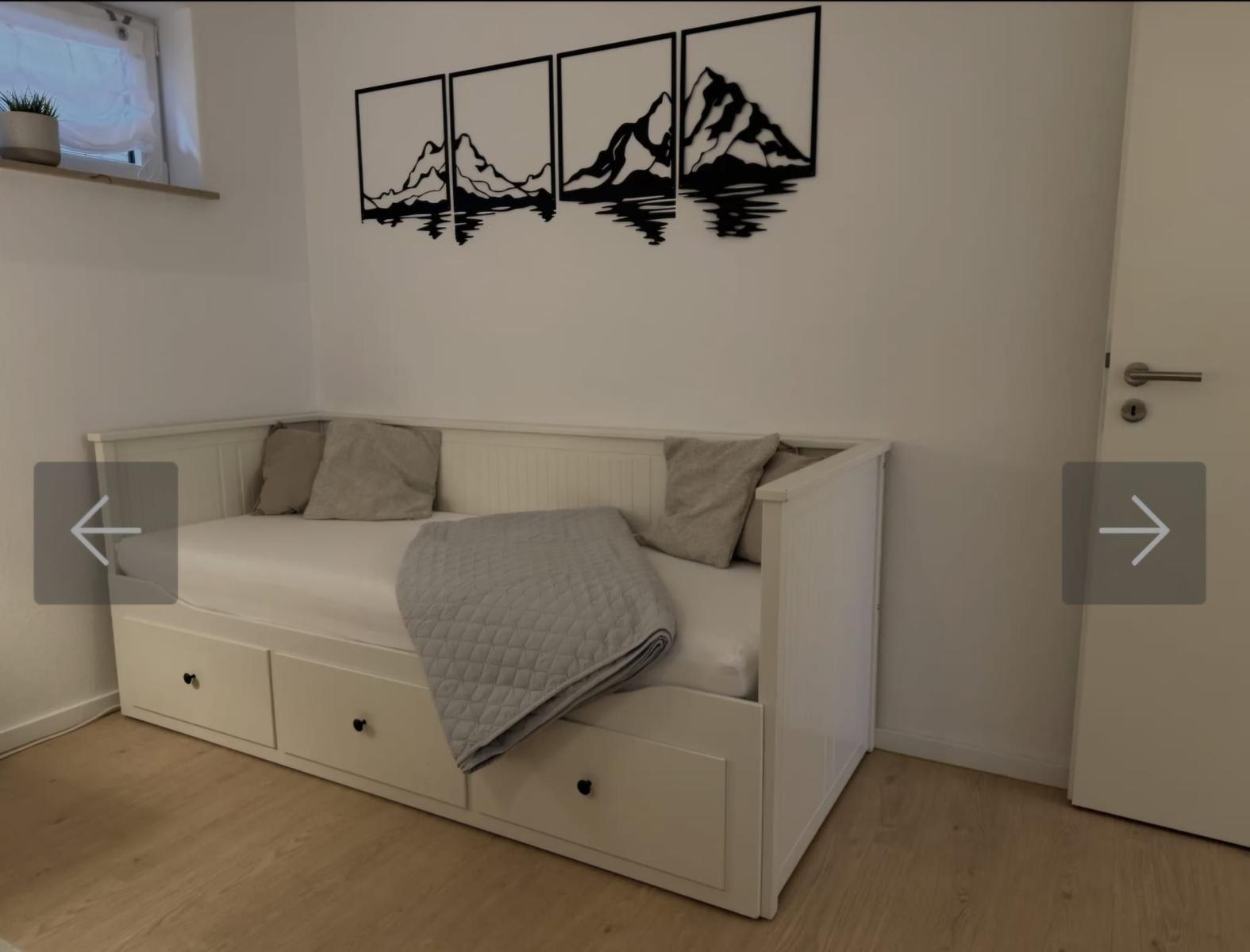Schlafzimmer mit weißem Bett, Wandbild und Holzboden.