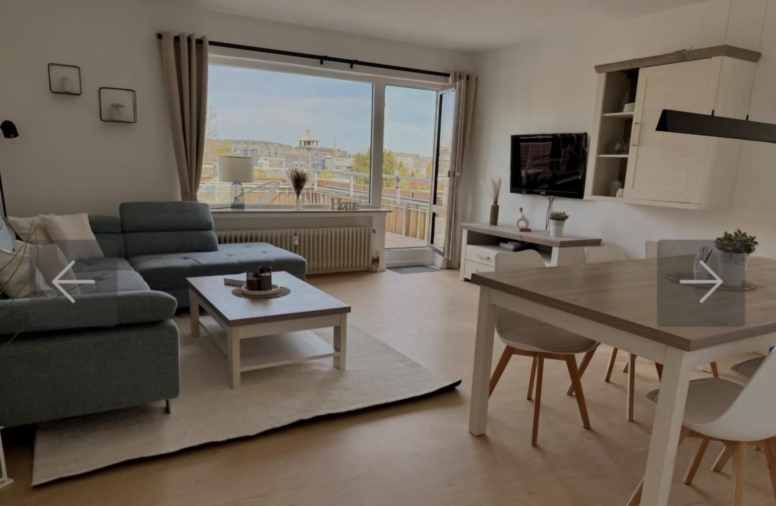 Wohn- und Essbereich mit Balkon, Sofa, Esstisch und Fernseher.