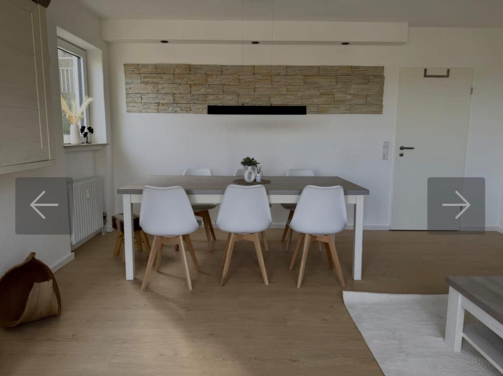 Esszimmer mit Tisch, Stühlen und Steinwand im Hintergrund.