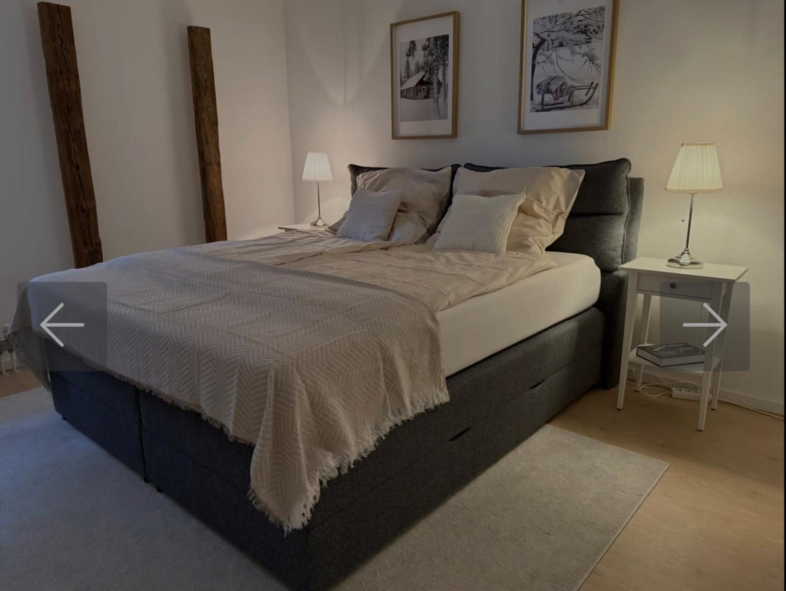 Schlafzimmer mit Bett, Nachttischen und Wandbildern.