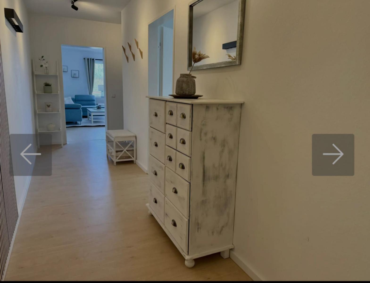 Flur mit Schrank und Spiegel. Im Hintergrund ist das Wohnzimmer mit blauem Sofa sichtbar.