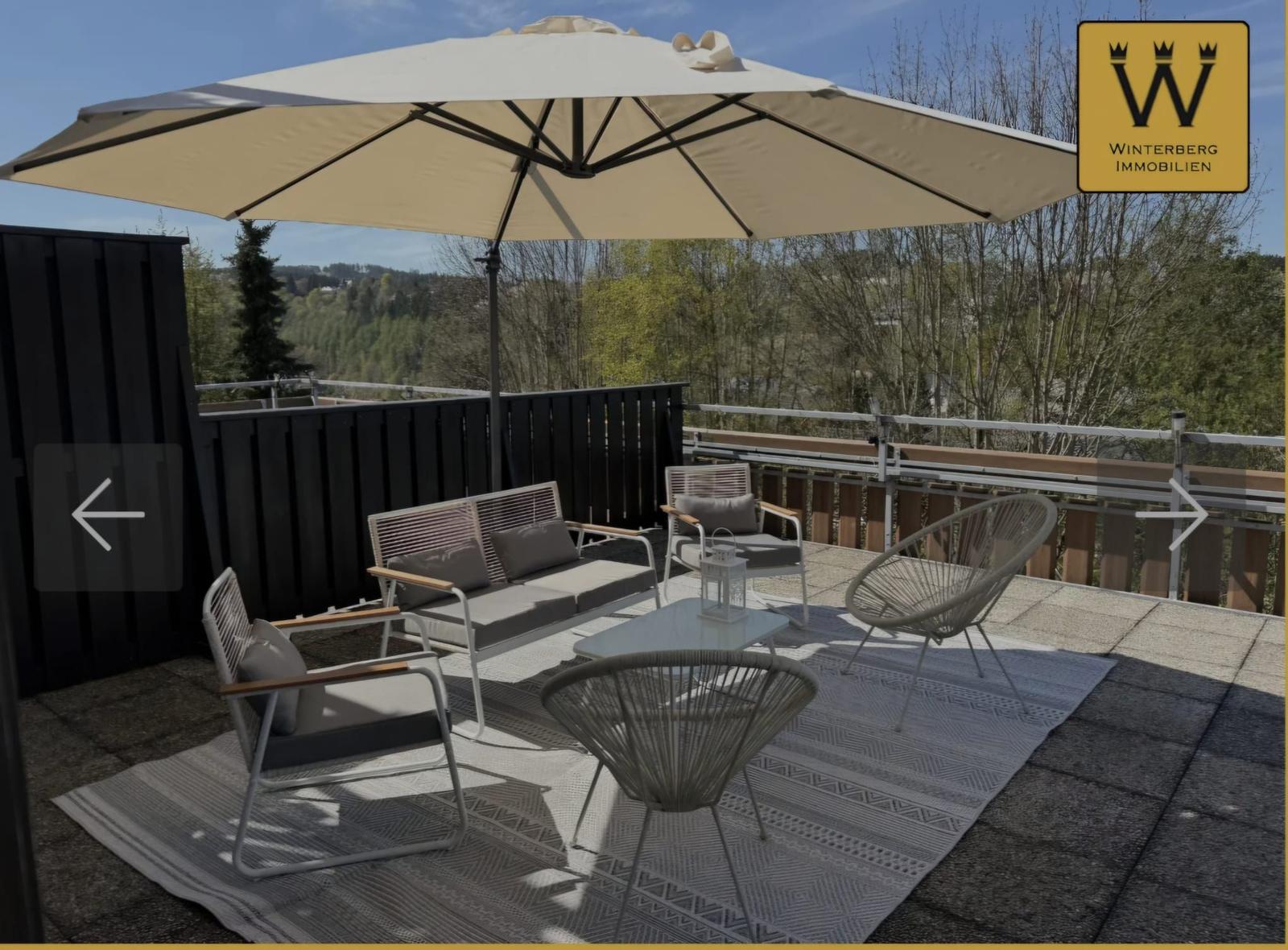 Terrasse mit Sitzgruppe, Sonnenschirm und Blick auf Wald.
