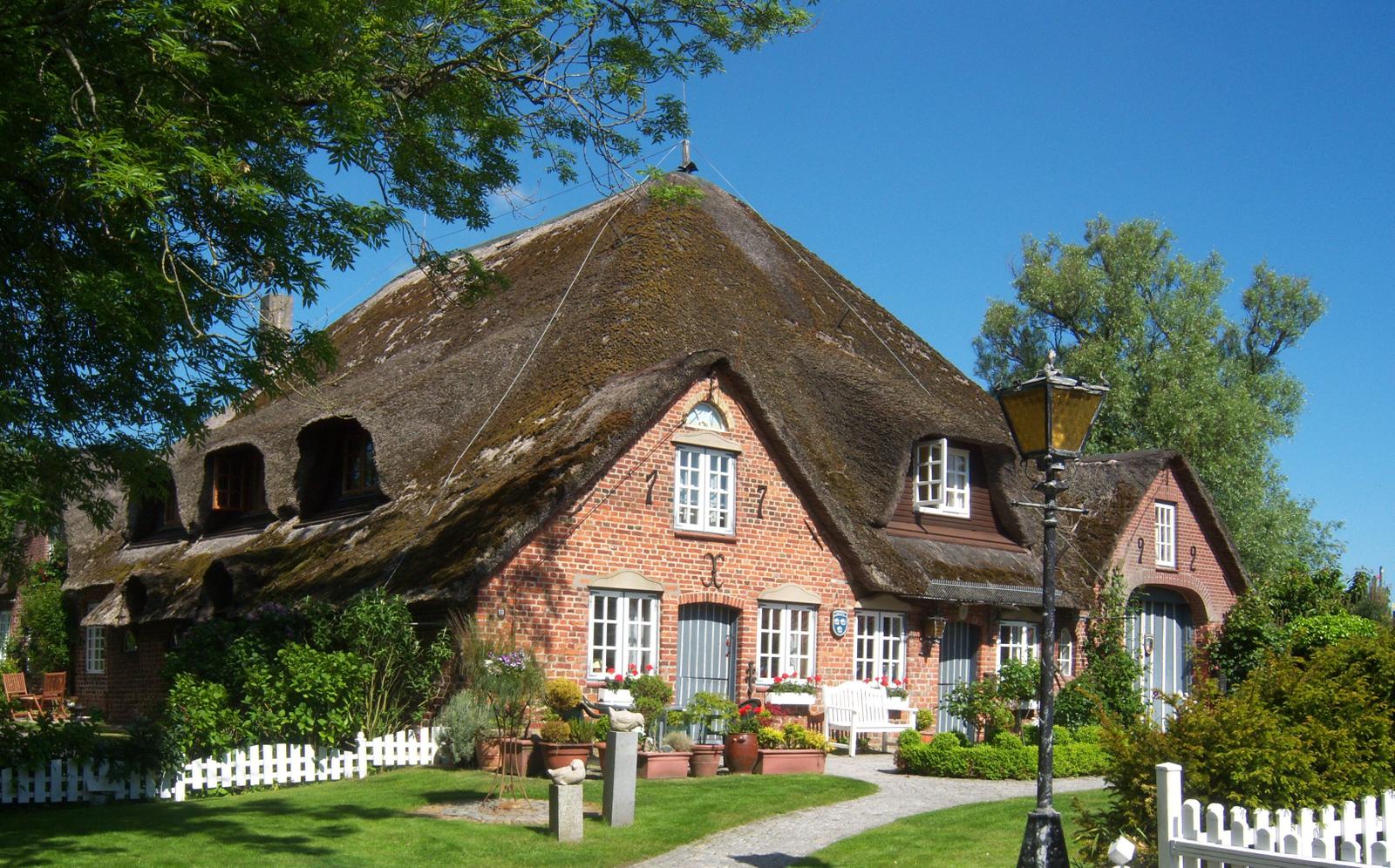 Red brick house with thatched roof and white garden fence.