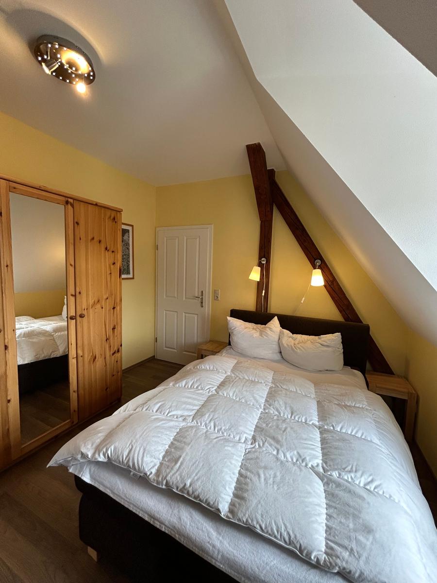 Schlafzimmer mit Dachschrägen, Holzbalken, Bett und Kleiderschrank.