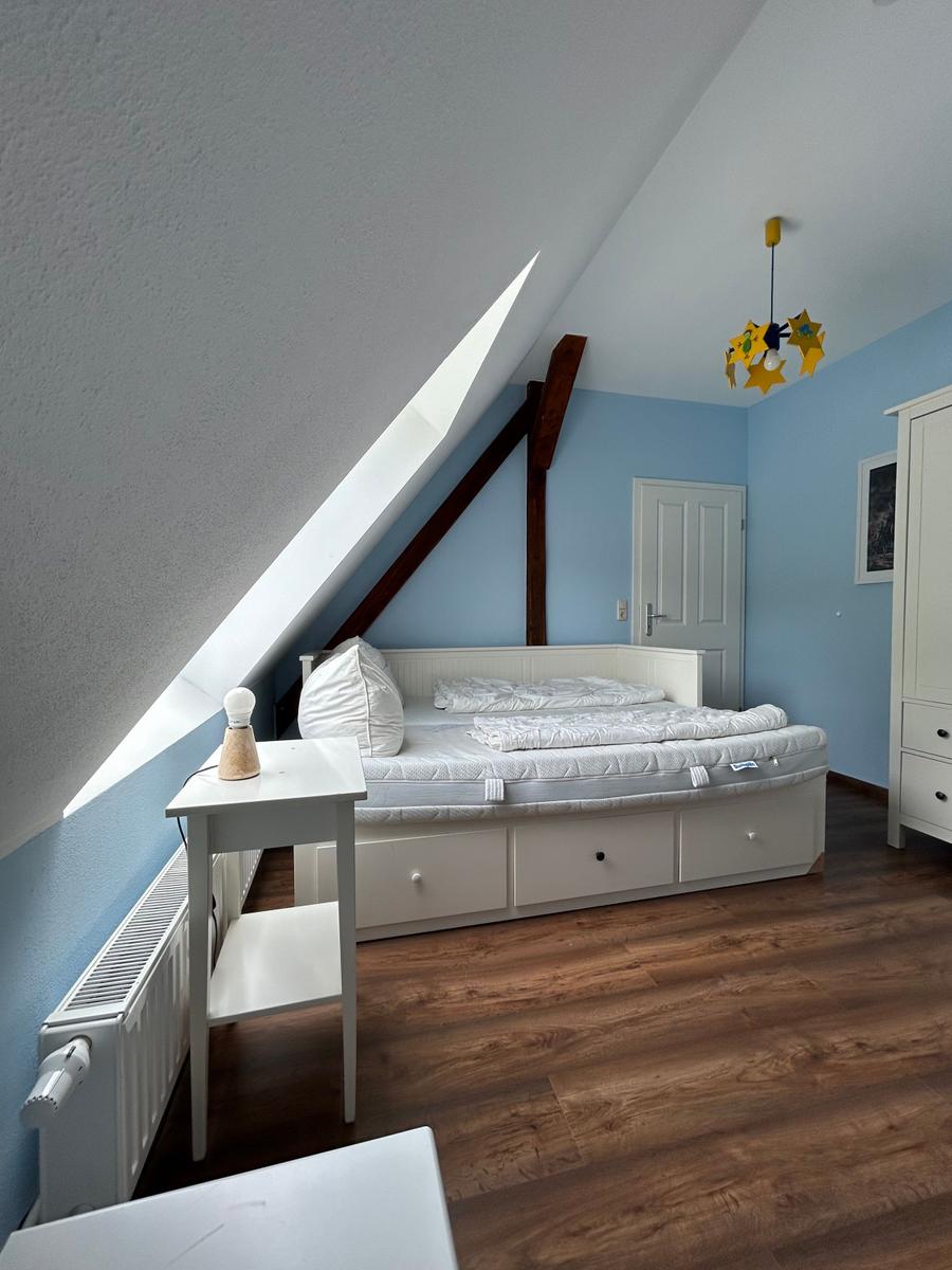 Schlafzimmer mit Dachschräge, weißem Bett und Holzboden.