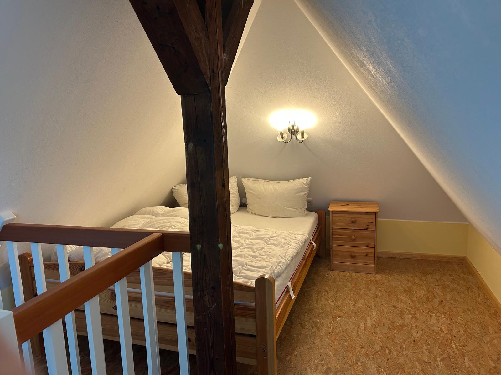 Schlafzimmer mit Dachschräge, Holzbett, Nachttisch und Wandlampe.